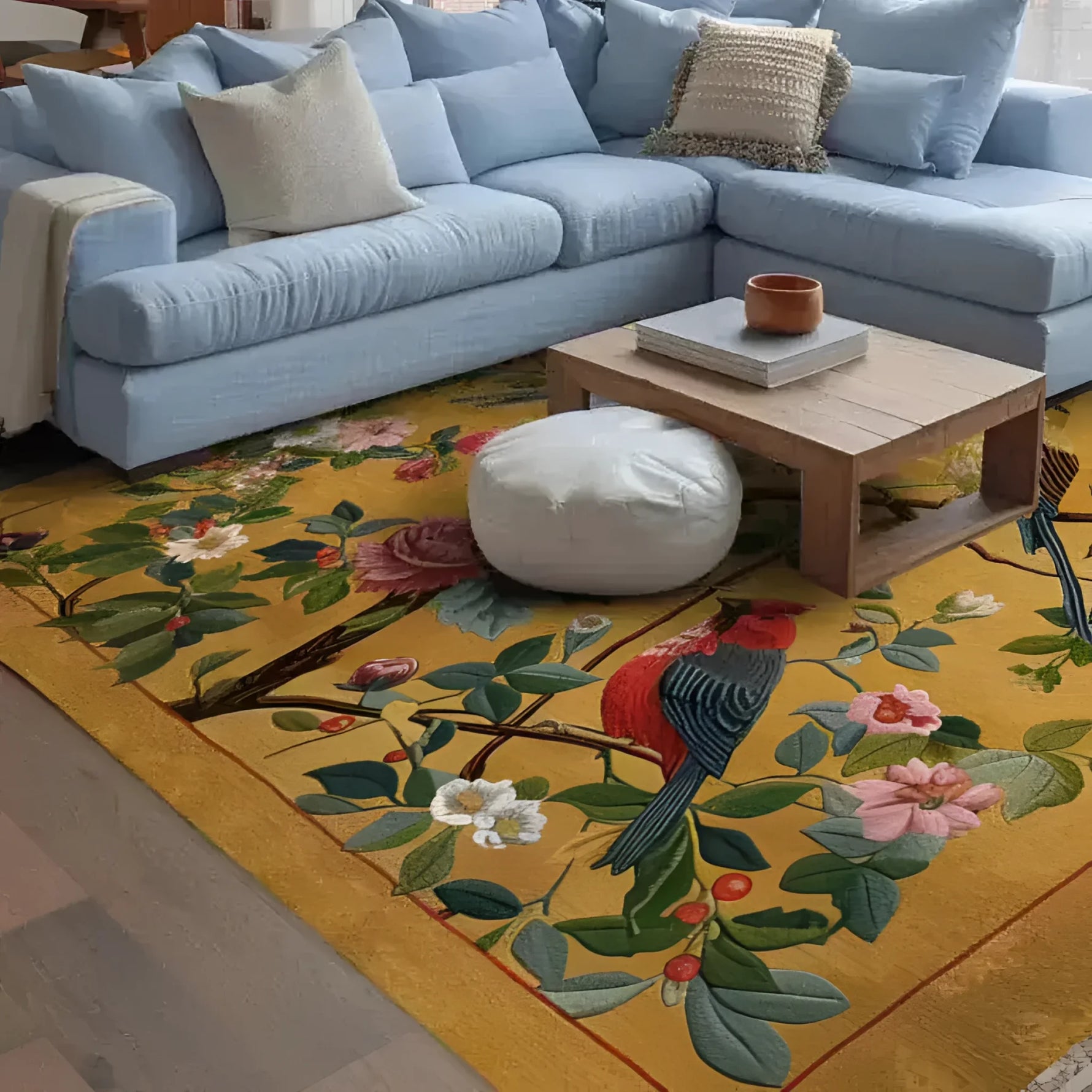 A vibrant Emperor's Loom Hand Tufted Area Rug adorns a cozy living room, featuring a detailed floral and bird design on a warm yellow background. This wool rug complements a light blue sectional sofa and wooden coffee table, creating an inviting and stylish space for large living room settings.