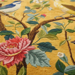 Close-up of tufted rug with floral and bird design on a yellow background