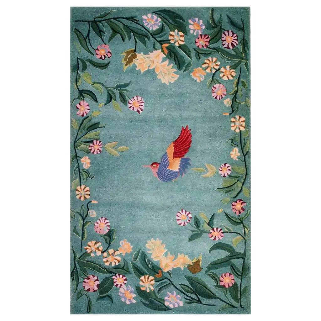 The Enchanted Floral Flight Knotted Wool Rug features a vibrant, hand-knotted design. A colorful hummingbird with red and blue wings is at the center, surrounded by a lush border of green leaves and multicolored flowers set against a soft blue background. This elegant area rug adds a touch of nature and whimsy to any space.