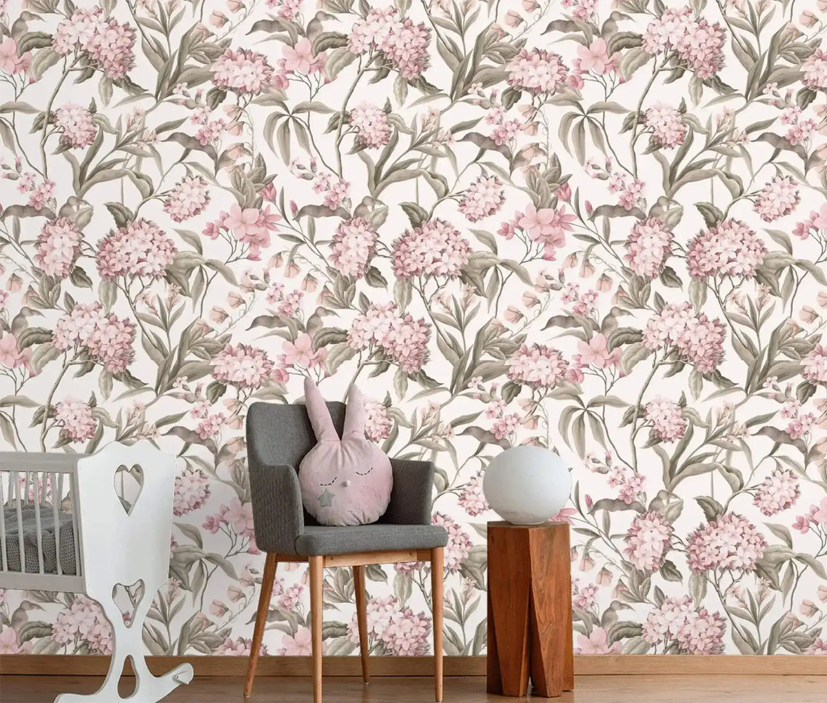 English Garden Wallpaper full-wall pink hydrangeas and taupe foliage behind gray nursery chair, white crib, wood table.