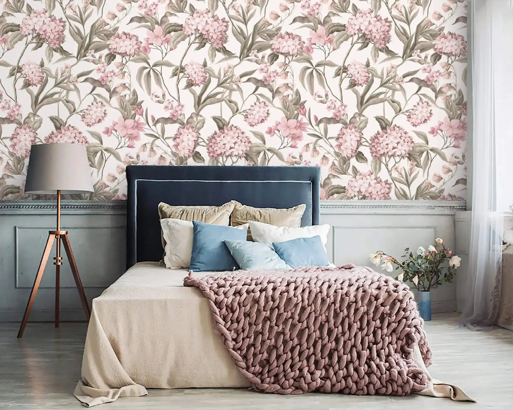 English Garden Wallpaper with large pink hydrangeas above a navy upholstered bed, pink knit throw, and tripod lamp.