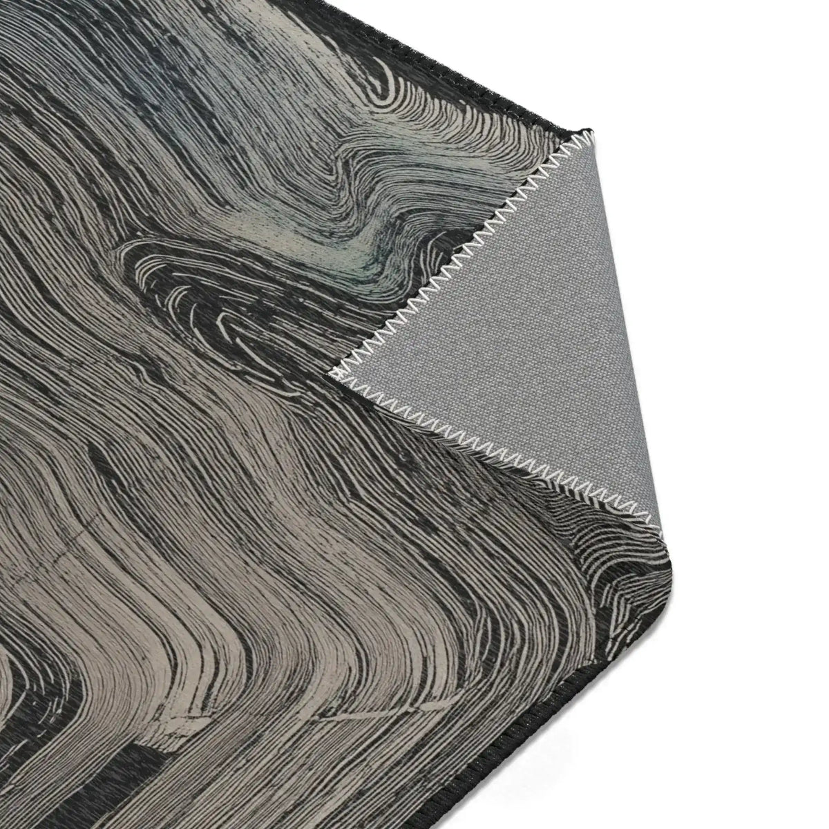 Corner detail of dark charcoal rug with swirling grey wave texture, folded corner reveals grey non-slip backing with zigzag stitching, Ethereal Archway Fluid Pathways Rug