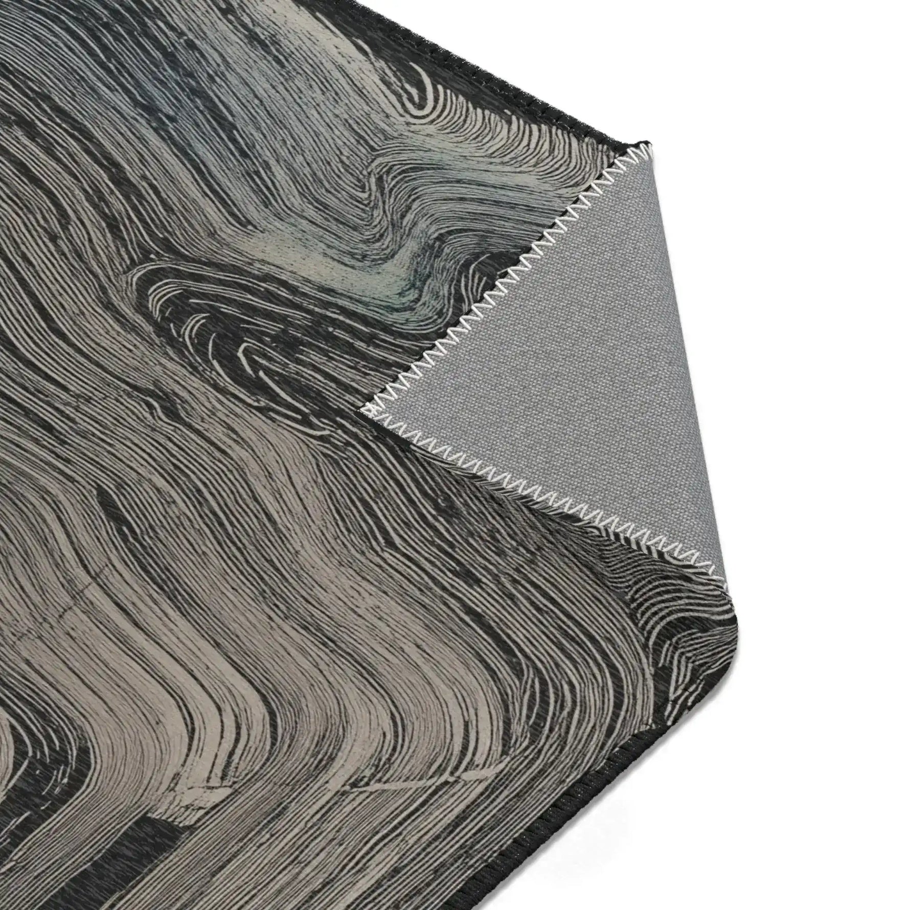 Corner detail of dark charcoal rug with swirling grey wave texture, folded corner reveals grey non-slip backing with zigzag stitching, Ethereal Archway Fluid Pathways Rug