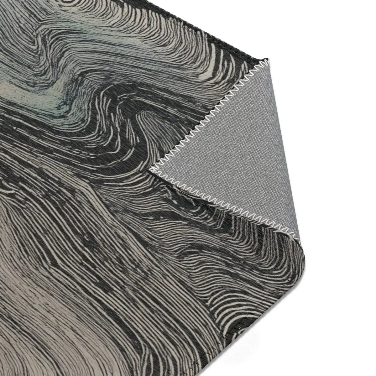 Folded corner showing charcoal surface with flowing grey wave line pattern and grey fabric backing with overlock stitching on the Ethereal Archway Fluid Pathways Rug