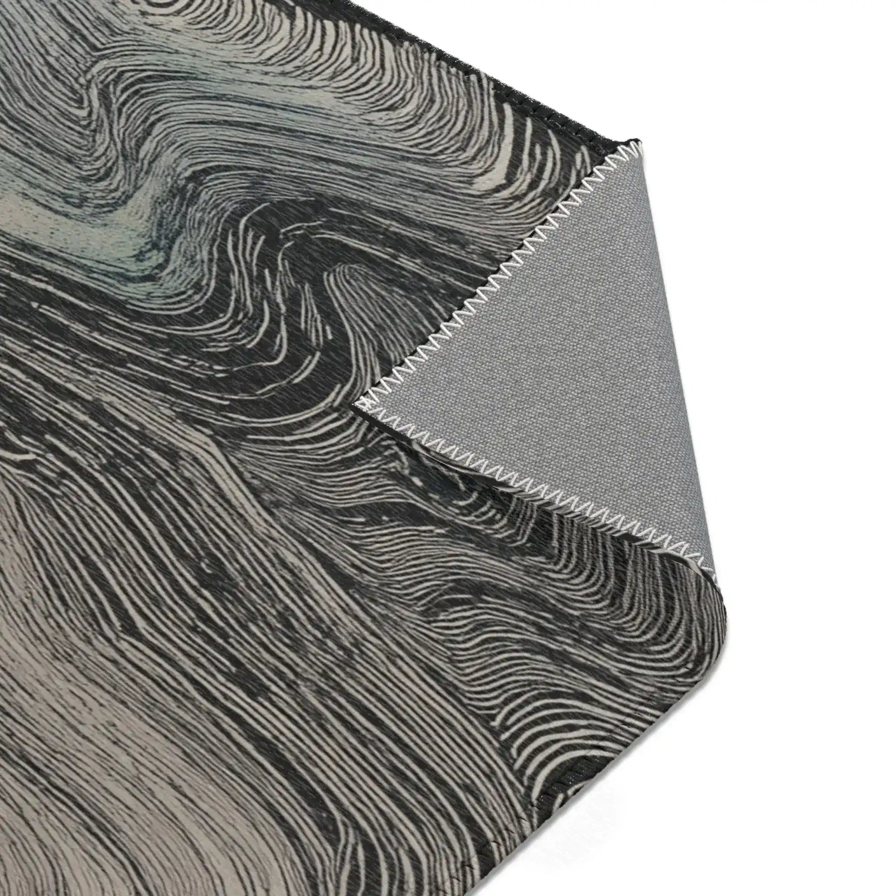 Folded corner showing charcoal surface with flowing grey wave line pattern and grey fabric backing with overlock stitching on the Ethereal Archway Fluid Pathways Rug
