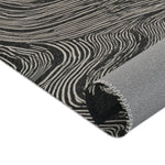 Rolled corner edge of the Ethereal Archway Fluid Pathways Rug in black and cream fluid stripe wave pattern with grey backing visible and overlock trim