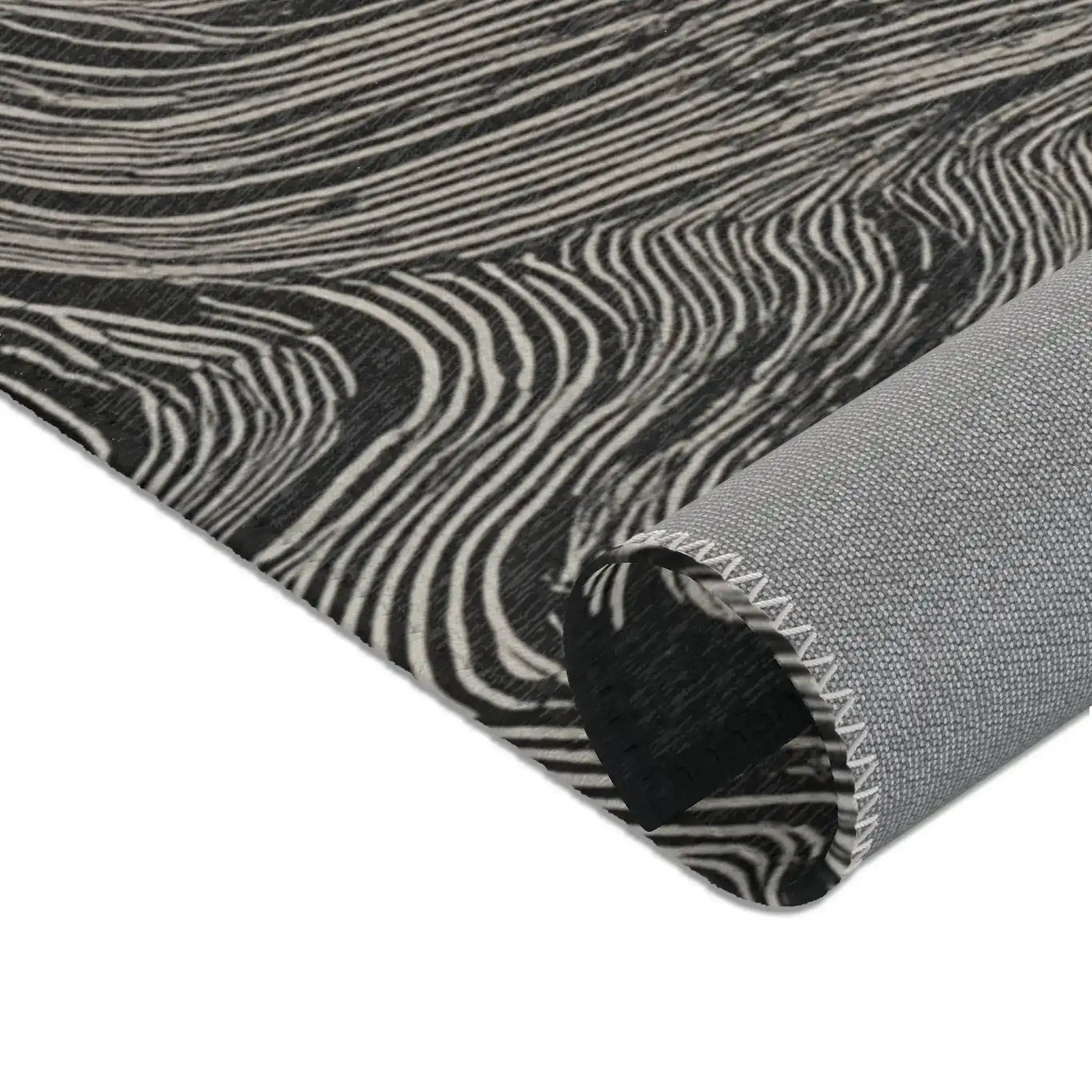 Rolled corner edge of the Ethereal Archway Fluid Pathways Rug in black and cream fluid stripe wave pattern with grey backing visible and overlock trim