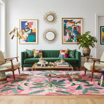 Living room with a green sofa, colorful pillows, and a pink rug with leaf patterns.