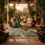 Woman in a green dress sitting in a luxurious room with floral rug and a fountain.