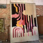 Abstract art rug piece on a wall with colorful patterns in a rustic setting.