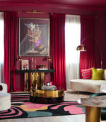 Modern living room with red curtains, colorful rug, and stylish furniture.