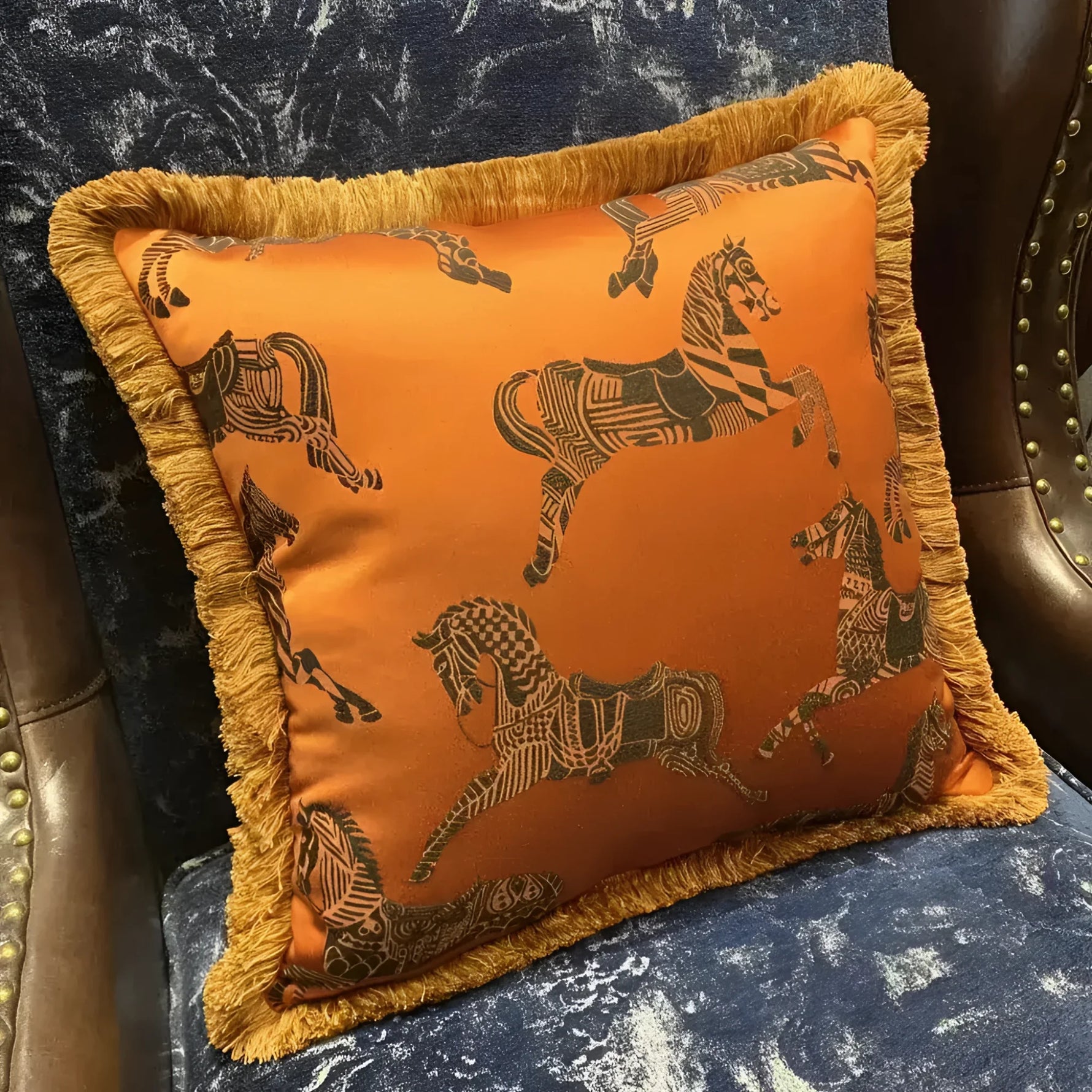 Faux silk throw pillow in vibrant orange with intricate horse pattern and golden fringes, perfect for adding a touch of elegance to your home decor.