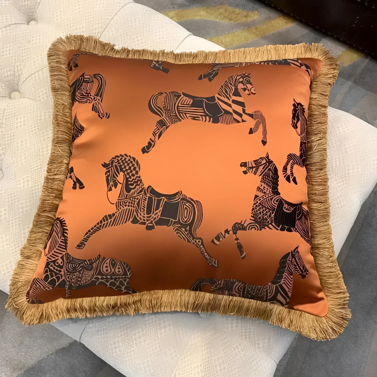 Faux silk throw pillow featuring a vibrant orange color with intricate black horse patterns and decorative golden fringes, perfect for home decor.