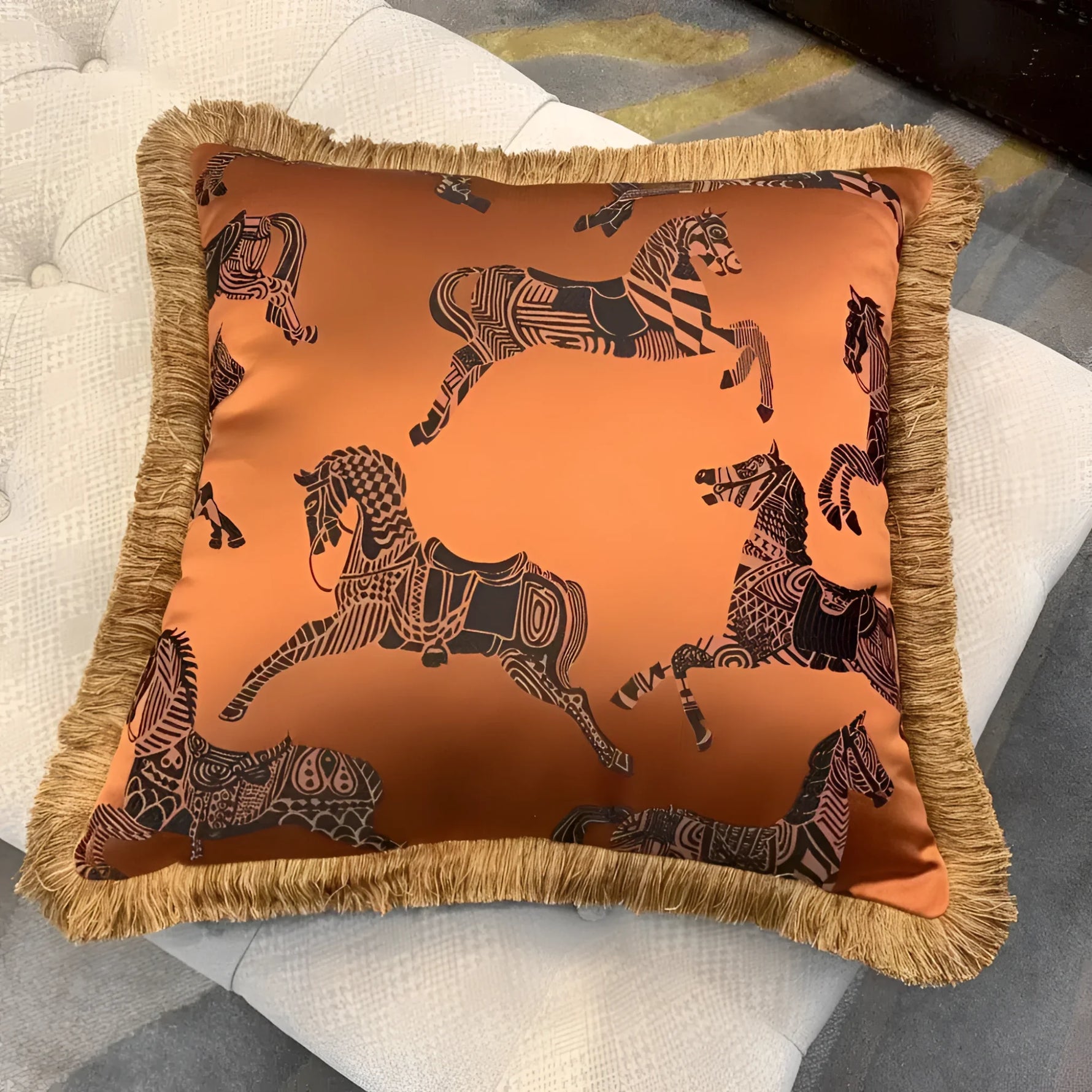 Faux silk throw pillow featuring a vibrant orange color with intricate black horse patterns and decorative golden fringes, perfect for home decor.