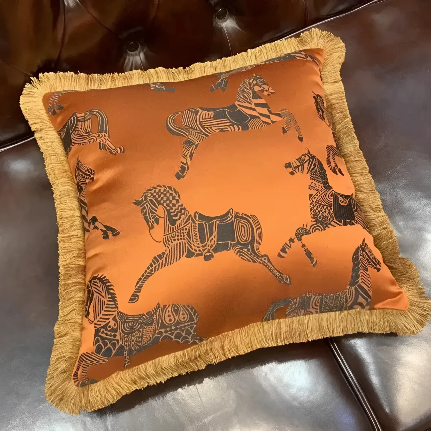 Faux silk throw pillow featuring orange fabric with intricate black horse designs and golden fringes, perfect for home decor.