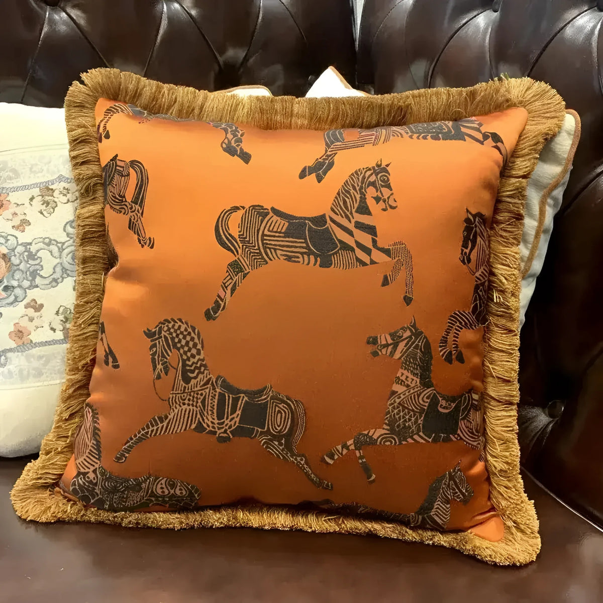 Faux silk throw pillow featuring an orange background with black horse patterns and golden fringes, perfect for adding a touch of elegance to your home decor.
