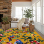A vibrant, hand-tufted wool area rug featuring colorful birds and flowers on a yellow background, beautifully placed in a cozy living room. The living room area rug complements the neutral-toned furniture and natural light streaming through large windows, creating a warm and inviting atmosphere.