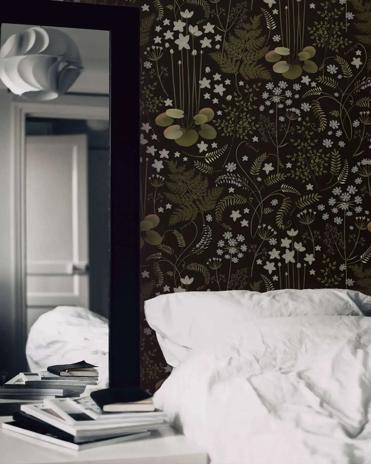 Fern blossoms monochrome wallpaper in moody bedroom with white pillows and a tall black mirror reflecting the room