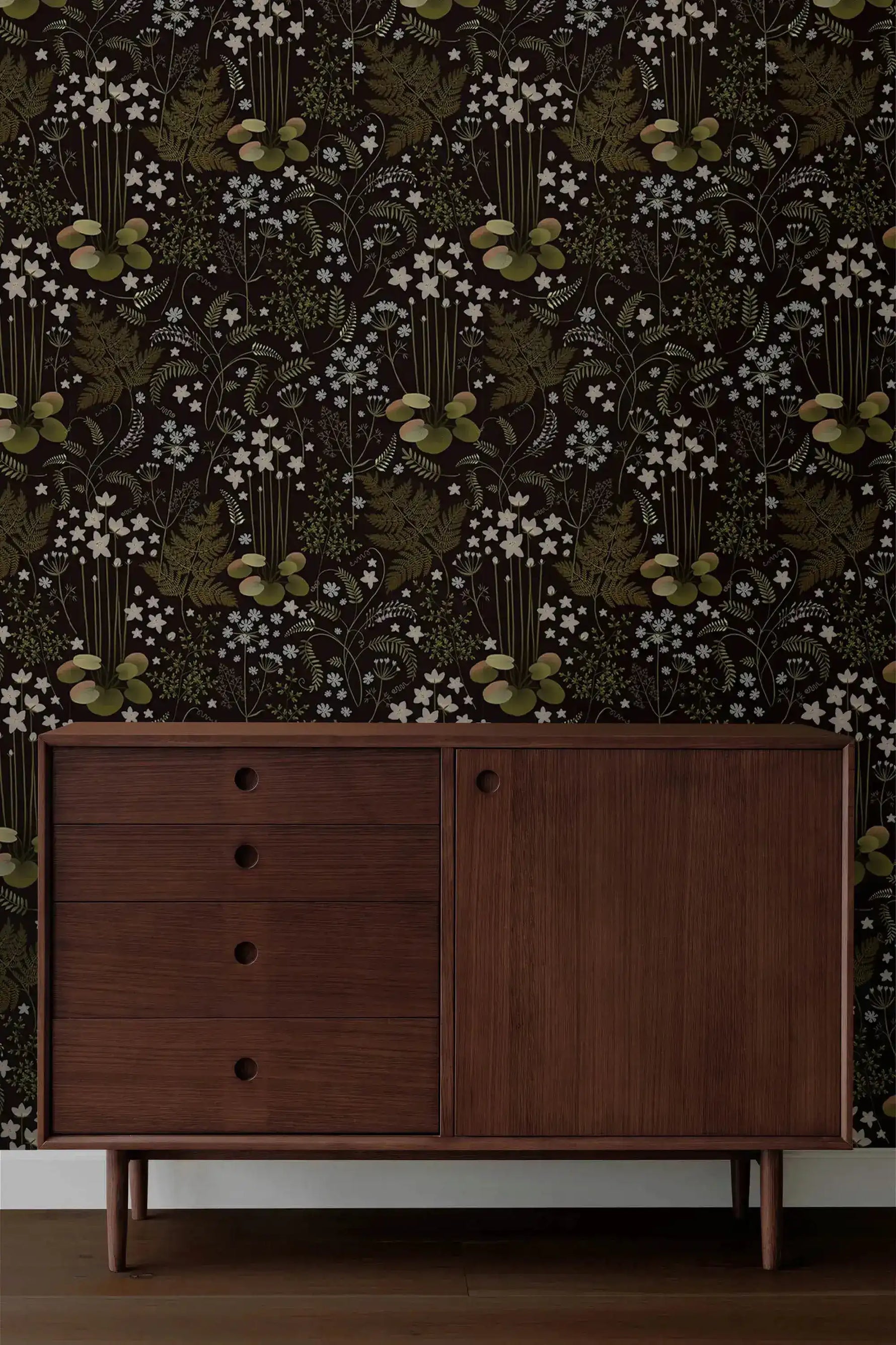 Fern blossoms monochrome wallpaper behind a dark walnut mid-century sideboard with round drawer pulls