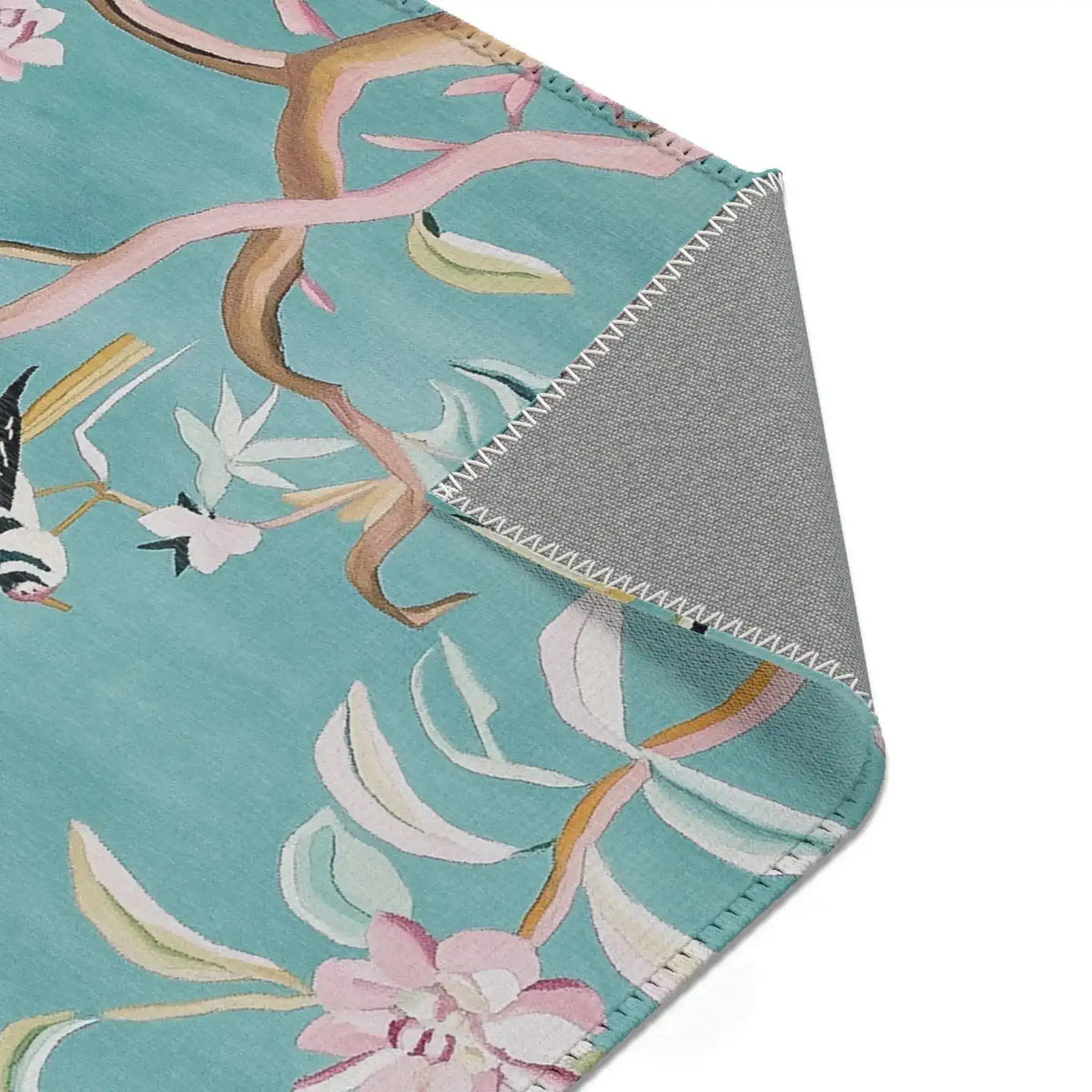 Top corner of teal Floral Birds Accent Rug folded back displaying bird and branch motif, grey backing, zigzag stitching