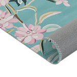 Bottom corner of teal Floral Birds Accent Rug showing pink blossoms and grey non-slip backing curled at corner