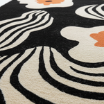 Close-up of a rug with abstract patterns in black, white, and orange.