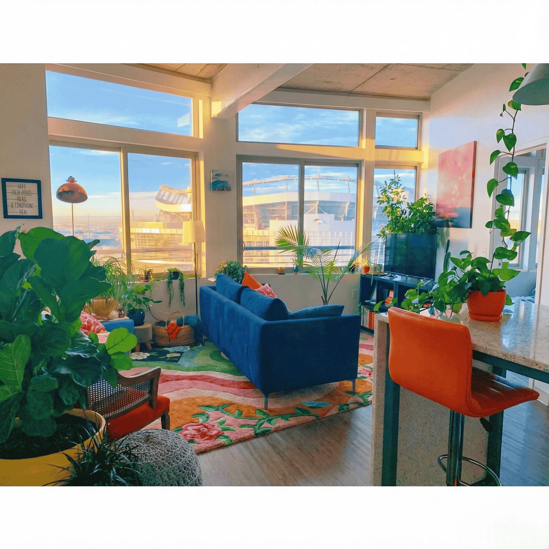 Modern living room with blue sofa, orange chair on a rug and large windows.