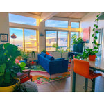 A vibrant living room featuring a Floral Wavefront Hand Tufted Area Rug. This wool rug, sized 8x10, showcases a colorful floral design that adds elegance to the space. Surrounded by lush plants, a blue sofa, and a modern decor, it enhances both the living room and dining room aesthetics.
