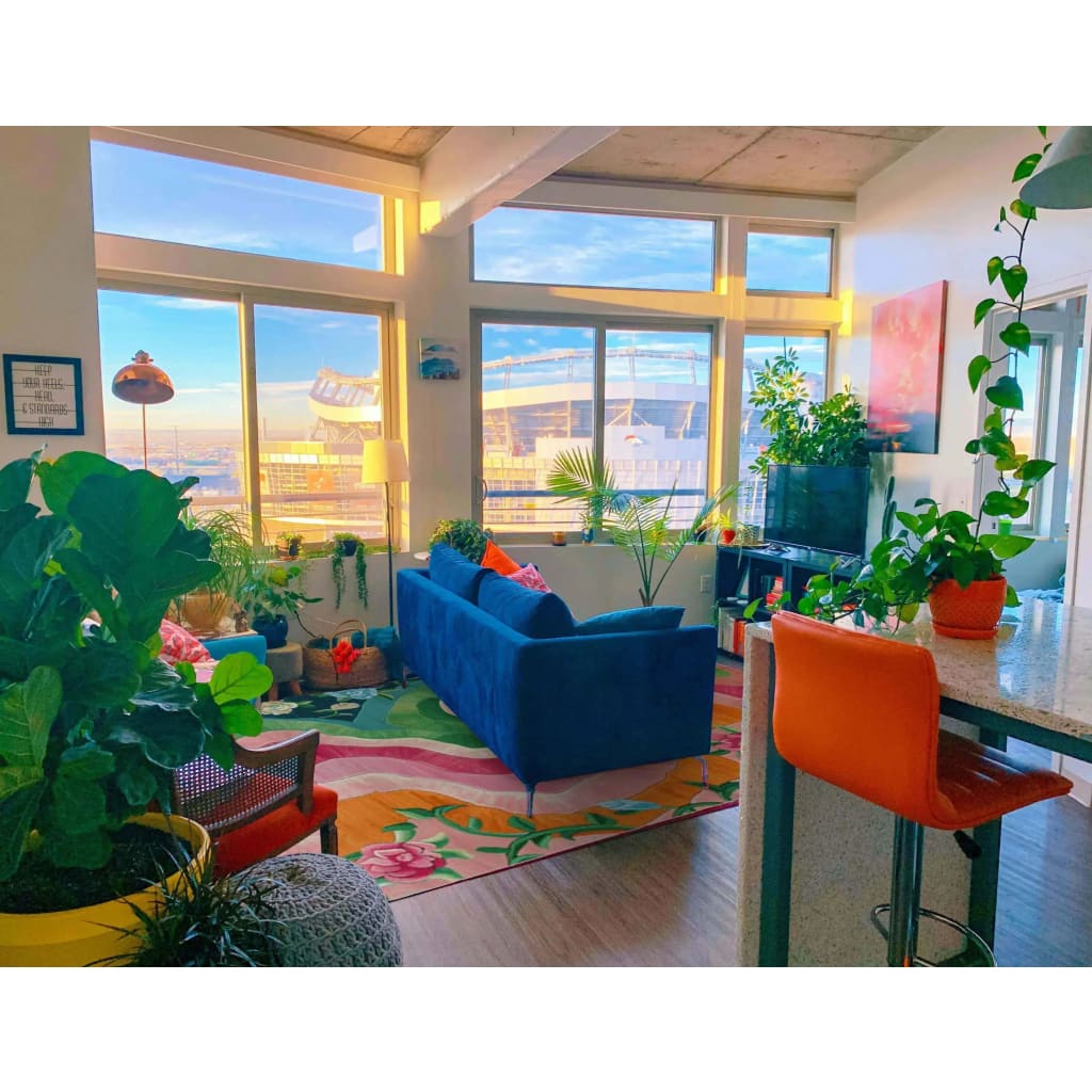 A vibrant living room featuring a Floral Wavefront Hand Tufted Area Rug. This wool rug, sized 8x10, showcases a colorful floral design that adds elegance to the space. Surrounded by lush plants, a blue sofa, and a modern decor, it enhances both the living room and dining room aesthetics.