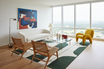 Modern living room with a white sofa, yellow armchair, and wooden chairs on a green rug.