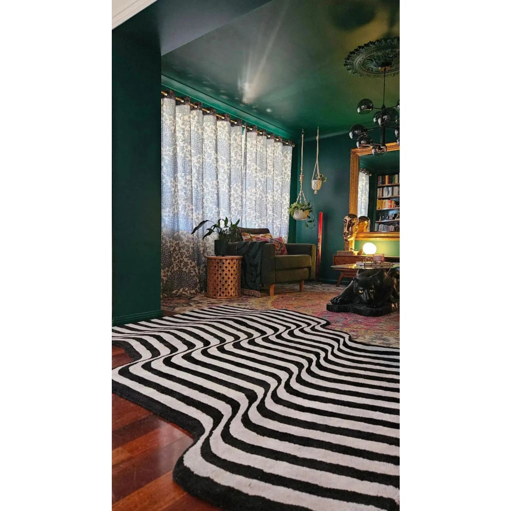 A stylish living room featuring a Flowing Illusion Black and Gray Wool Runner Rug with bold abstract patterns. The area rug complements the vintage decor, including a cozy armchair, decorative plant, and intricate wall art. Ideal for a contemporary living room, hallway runner, or as a kitchen rug, this wool rug adds a touch of sophistication and warmth.