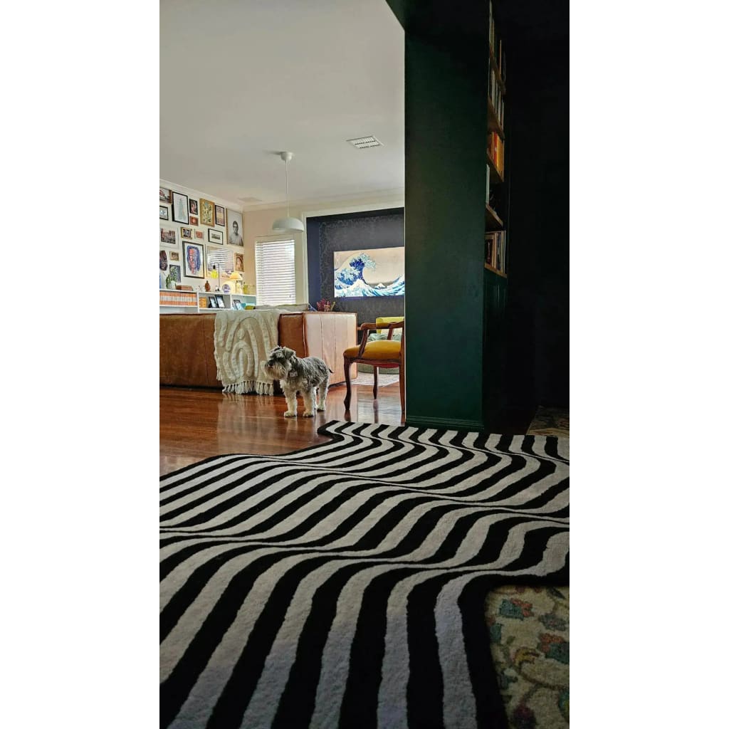 A stylish living room featuring the Flowing Illusion Black and Gray Wool Runner Rug with bold black and gray stripes, perfect as an area rug for contemporary spaces. This vintage rug elegantly complements the decor of a cozy living room, enhancing the charm of wooden flooring and eclectic wall art. Ideal for use as a hallway runner rug or in a large living room setting.