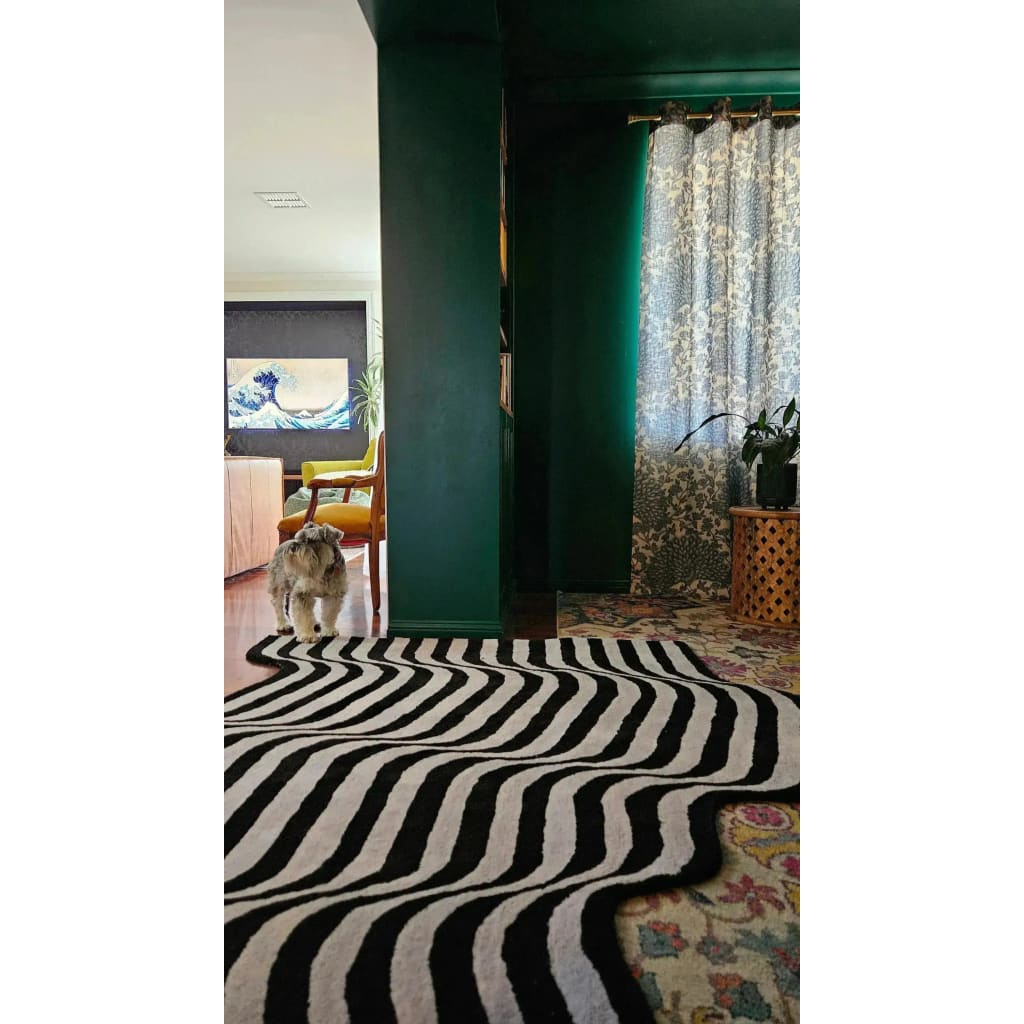 A stylish contemporary area rug in a black and gray flowing pattern graces a living room with dark green walls. The wool runner rug adds a touch of vintage charm, perfect for use as a hallway runner or in a large living room. A cozy scene with a small dog and patterned curtains enhances the warm, inviting atmosphere.