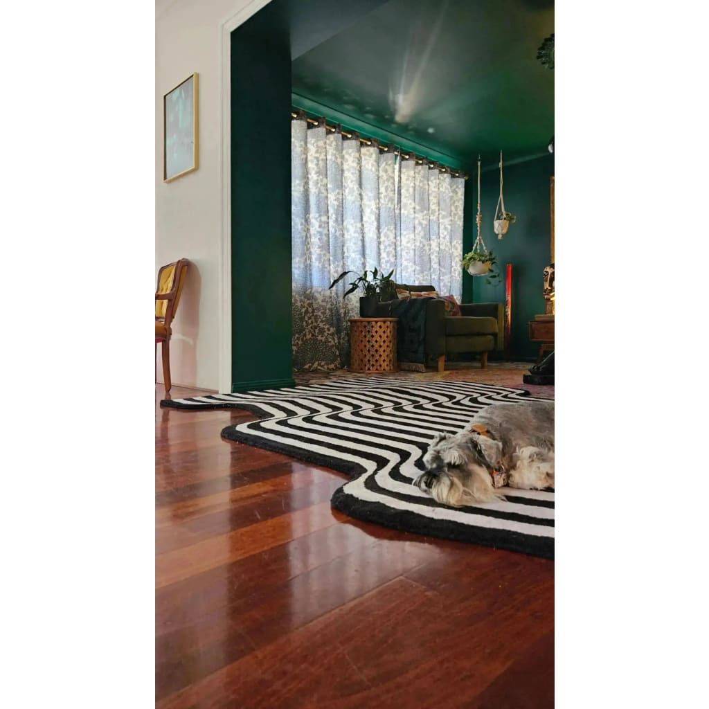 A stylish black and gray wool area rug with flowing patterns enhances the contemporary feel of a cozy living room. The vintage rug complements the dark green walls and wooden floor, making it an ideal choice for a hallway runner rug or a large living room rug. A small dog relaxes on the rug, adding a touch of warmth to the elegant setting.
