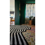 A stylish black and gray wool area rug with flowing illusion pattern adds a touch of contemporary elegance to the living room. The rug's bold design stands out against the vintage decor, making it ideal for dining rooms and hallways. Perfect as a kitchen runner rug or a large living room centerpiece, this wool rug complements both modern and traditional settings.