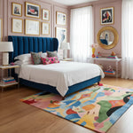 Decorative bedroom with a blue upholstered bed, colorful rug, and framed artwork on pink walls.
