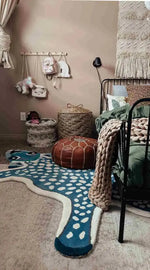 Charming bedroom setup featuring a For the Love of Deer hand-tufted wool rug in dark blue, designed with playful white spots, perfect for adding a whimsical touch to any bedroom or living room area. The cozy setup includes a woven basket, a leather pouf, and a plush knit blanket draped over a metal bed frame.