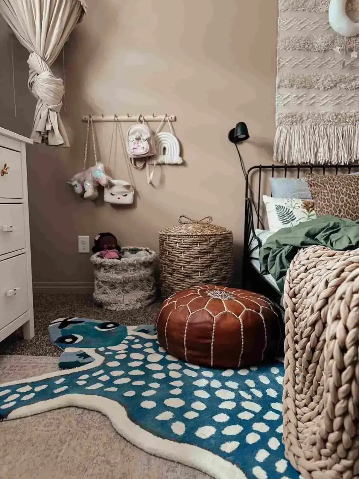 A cozy bedroom featuring a dark blue hand-tufted wool area rug with a playful deer design. The rug adds a touch of whimsy to the room, complementing the woven baskets, leather pouf, and neutral decor. Perfect for enhancing both bedroom and living room spaces.