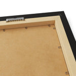 Back of framed poster showing MDF backing board, serrated metal hanging bracket and wire clips inside black frame