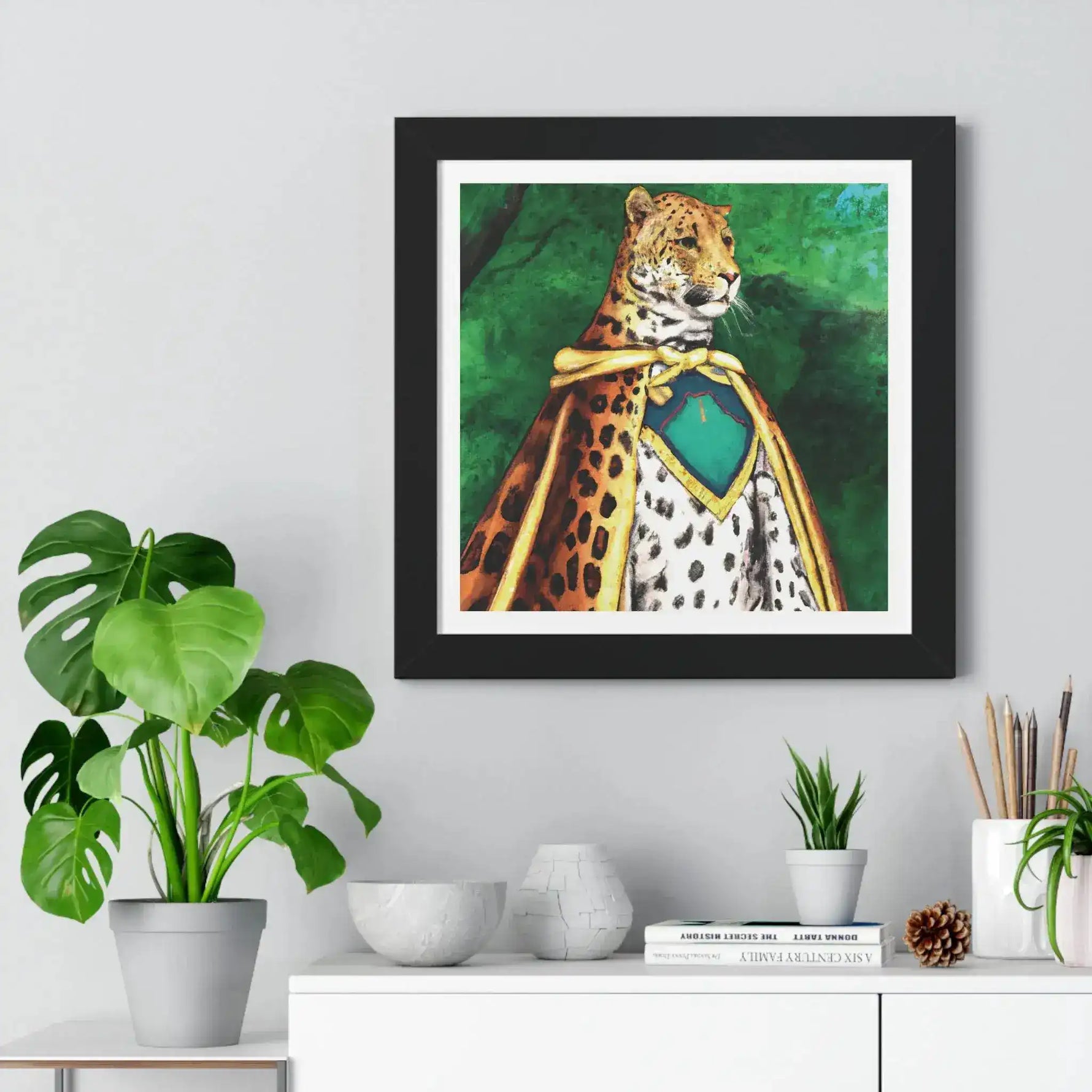 Framed horizontal poster in black frame, illustrated leopard in gold-trimmed cape on green jungle background, hung above console