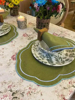 Garden Grove placemat on table, olive green scalloped oval with blue trim, leaf-print china, green napkin, candle centerpiece