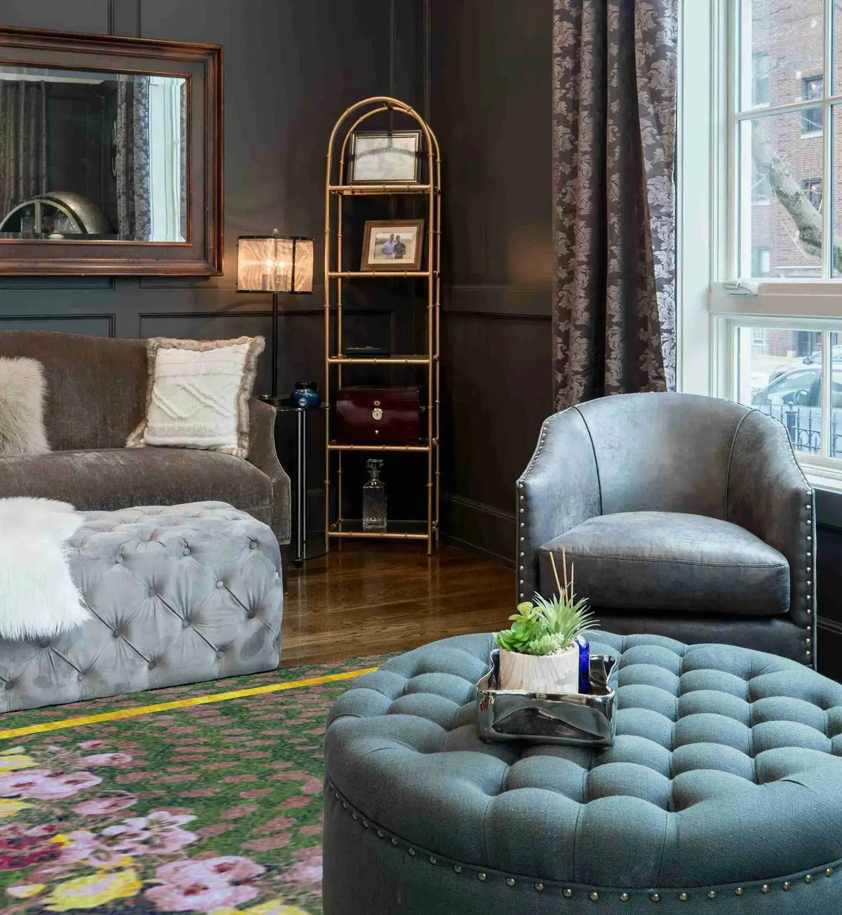 A stylish living room featuring the Garden of Courage Hand Tufted Rug in a night theme. This large area rug showcases a vintage design with a floral pattern, adding elegance to the space. The wool rug complements the sophisticated decor, including a tufted ottoman and plush seating, perfect for enhancing any living room area.