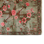This image showcases the Garden of Serein Knotted Wool Rug, a beautifully designed area rug perfect for living rooms. Featuring intricate floral patterns with pink blossoms on a soft green background, this wool rug adds elegance and warmth to any space.