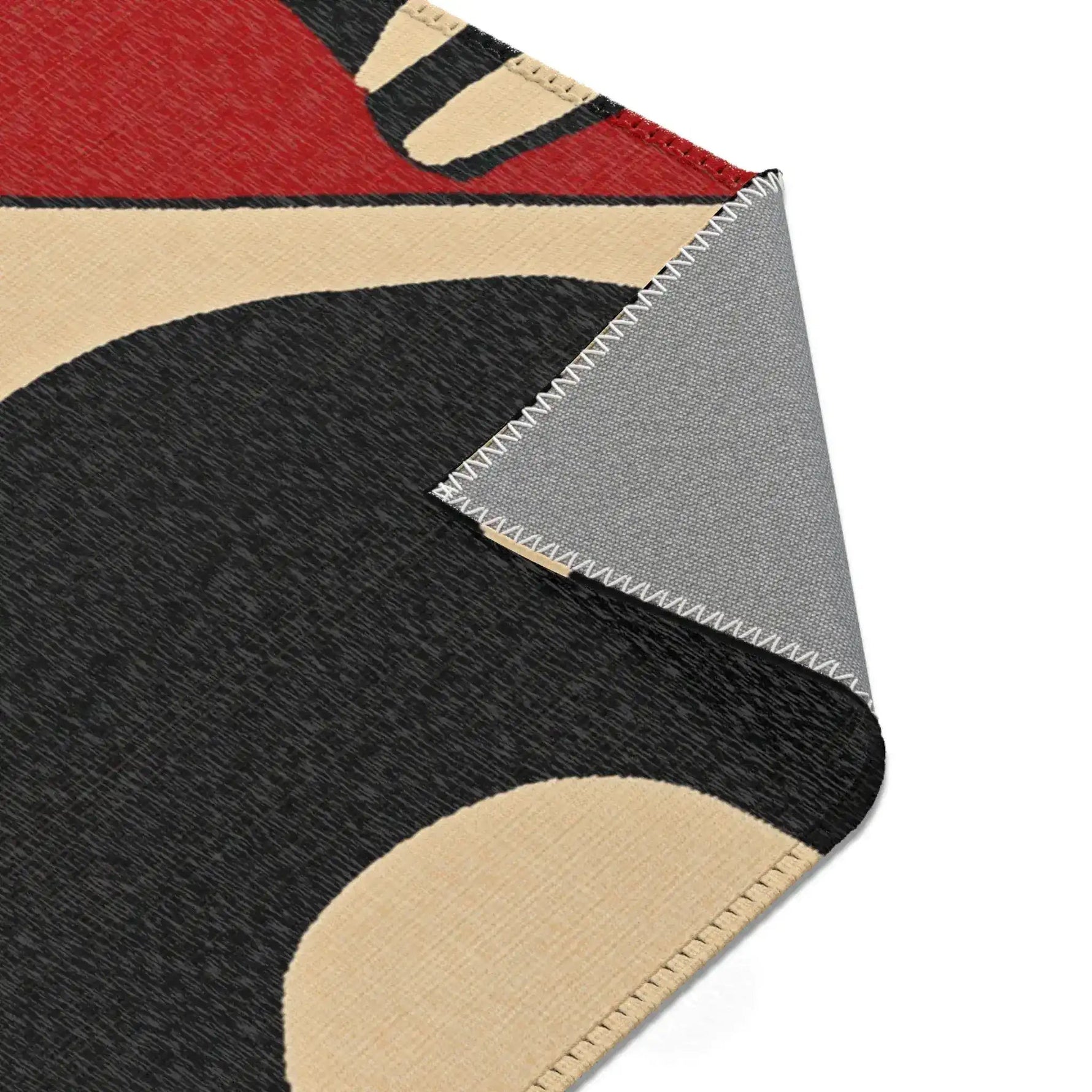 Corner turned back on Geometric Sunburst Accent Rug showing charcoal and cream sunburst face and grey backing with stitching