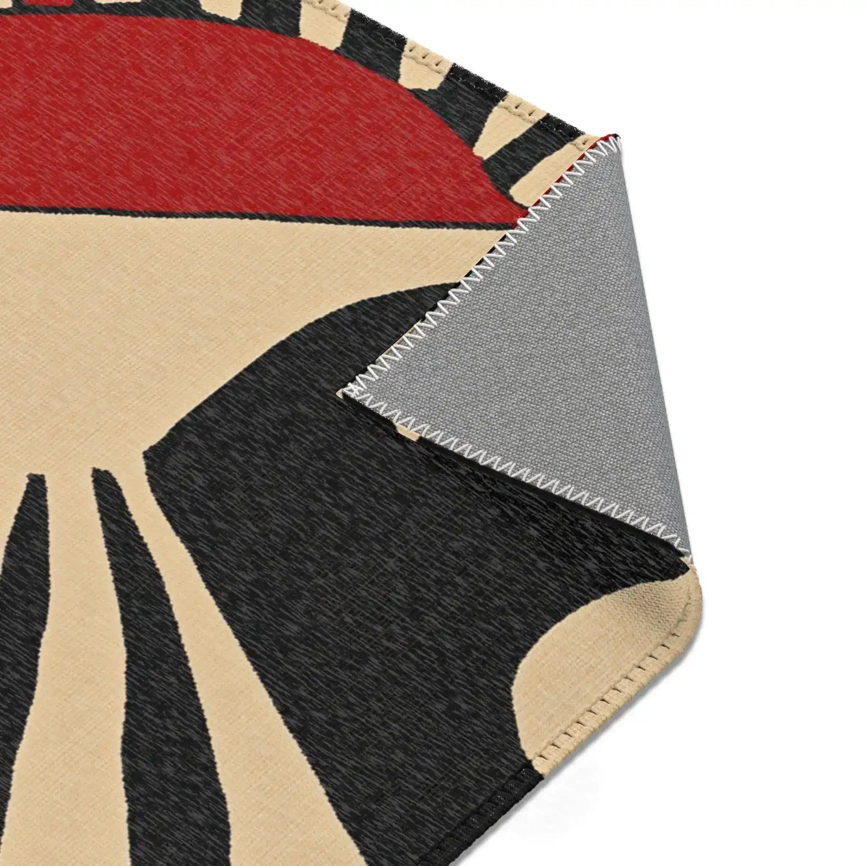 Corner fold of Geometric Sunburst Accent Rug showing cream black radial print and grey anti-slip backing with overlock stitching