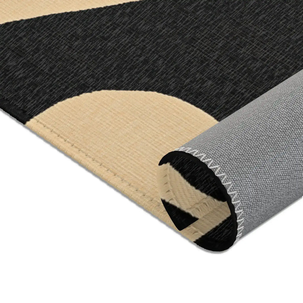 Rolled edge side view of Geometric Sunburst Accent Rug exposing grey anti-slip backing and overlock seam with cream black fabric