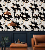 Gilded Petal wallpaper installed in living room, bold white gold-lined florals on black, copper pendant above leather chair