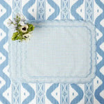 pale blue gingham placemat with scalloped edge, flat lay on ikat tablecloth with white anemone flower accent