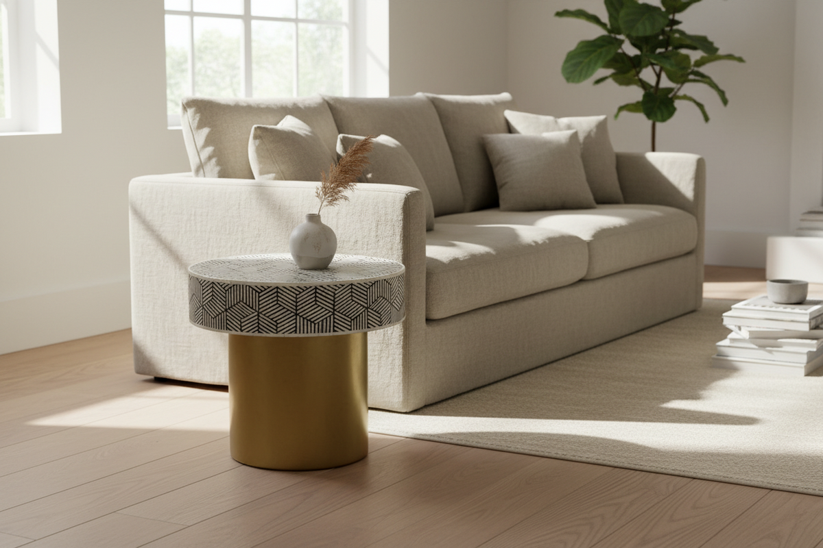Gold base bone inlay geometric round accent table with a patterned top beside a cream sofa.
