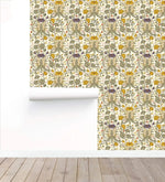 Roll of golden blooms floral wallpaper partially unrolled against a white wall on a bare wood floor